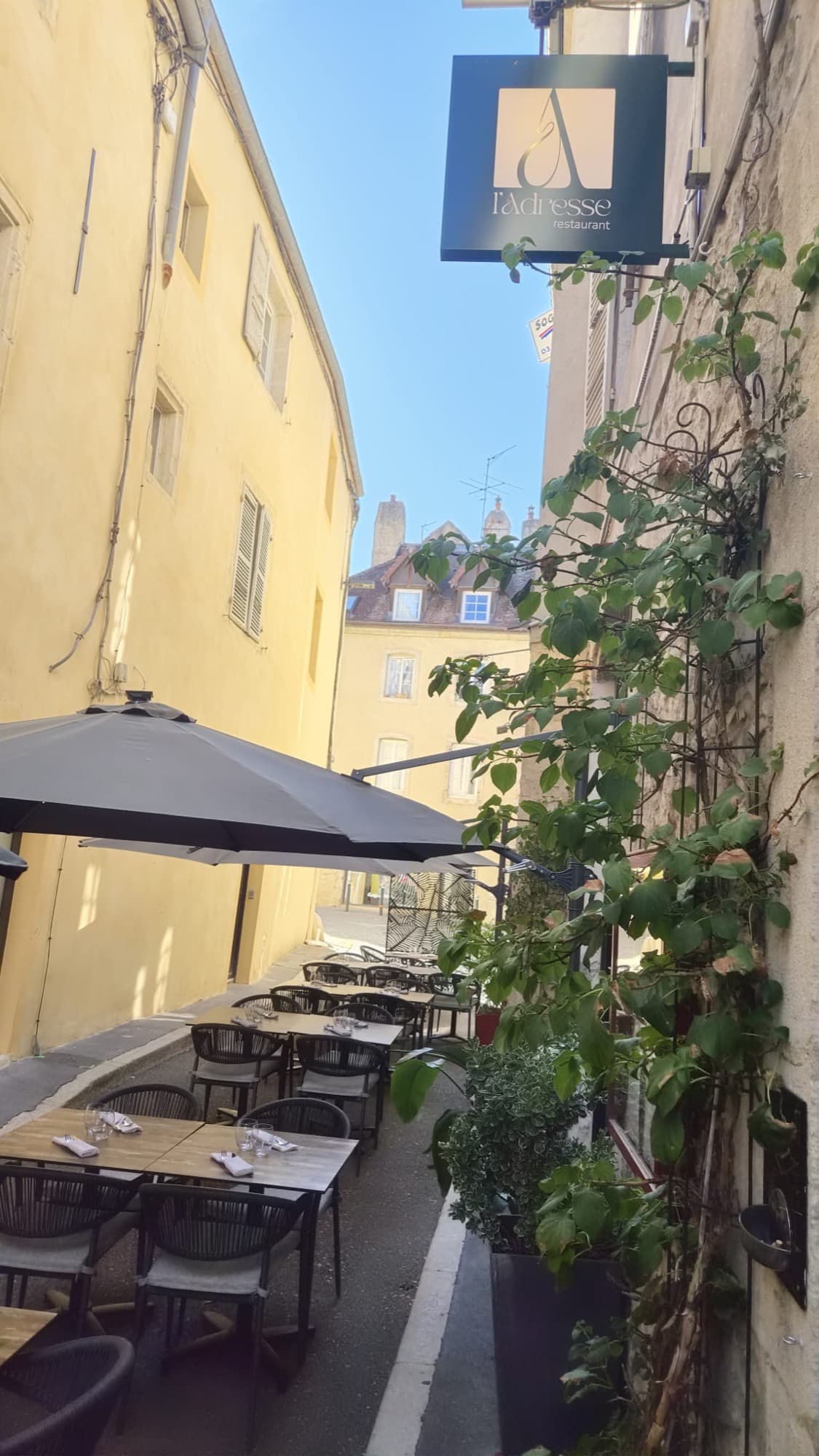 L'enseigne suspendue de L'Adresse au-dessus de la terrasse, dans la ruelle ensoleillée
